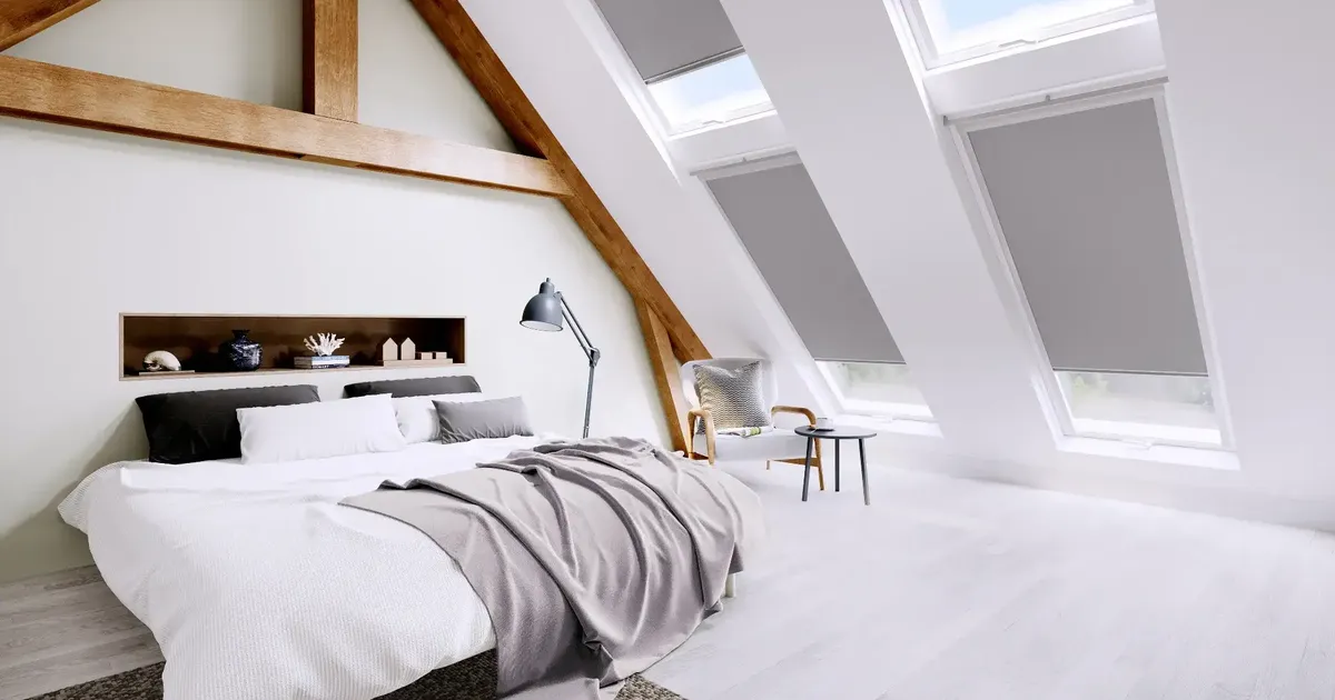 Bright attic bedroom with exposed timber beams and grey blinds fitted to three roof windows