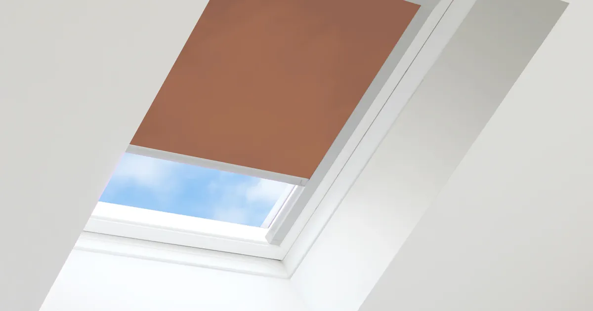 Close-up of a roof window with a Rust Translucent blind pulled part-way down in a silver frame